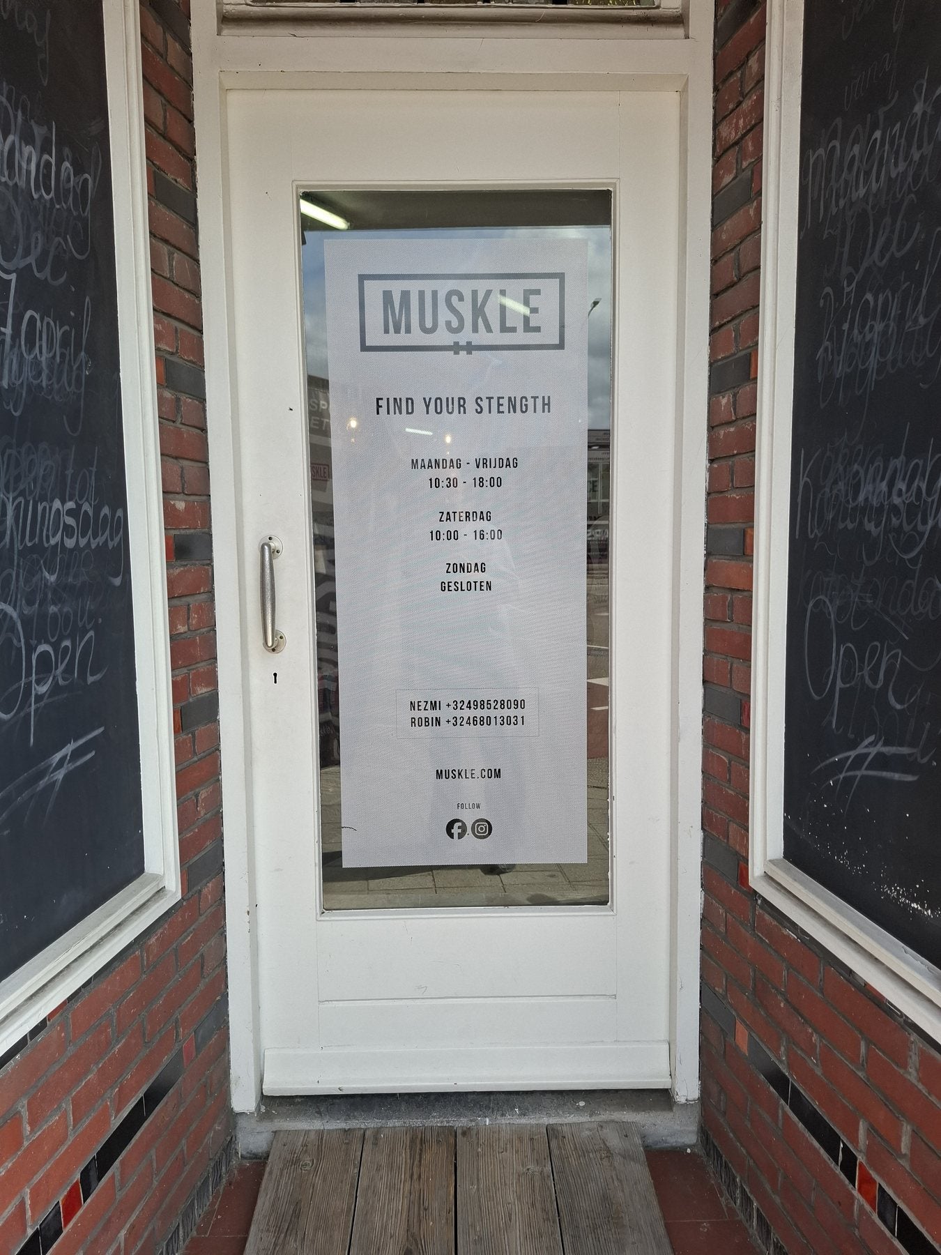 Ingangsdeur van MUSKLE Roosendaal met openingsurenposter