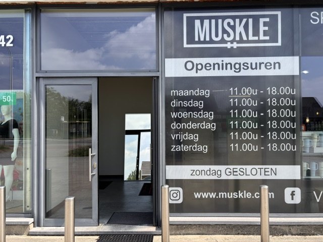 Glazen ingang van MUSKLE Begijnendijk met openingsuren op het raam