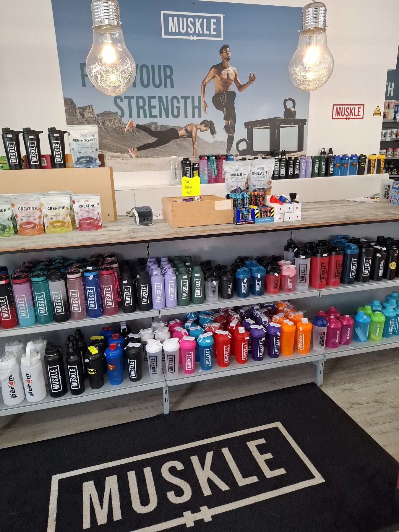 Servicebalie van MUSKLE Roosendaal met shakers en FUEL YOUR STRENGTH-banner